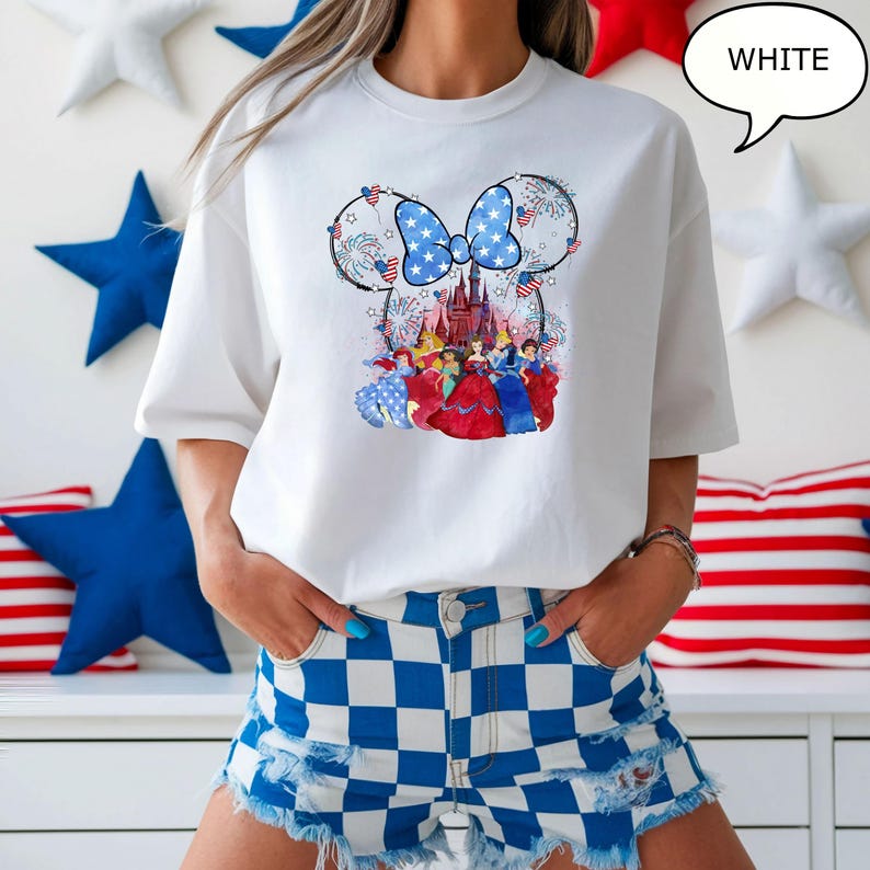 Puede incluir: Camiseta blanca con un dise&ntilde;o de Minnie Mouse con un lazo azul y un castillo. El dise&ntilde;o incorpora elementos de la bandera estadounidense y princesas de Disney. La palabra "WHITE" est&aacute; en una burbuja.