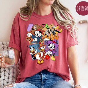 K&ouml;nnte beinhalten: Ein rotes T-Shirt mit einem Grafikdruck von Mickey Mouse, Minnie Mouse, Donald Duck, Goofy und Pluto in Halloween-Kost&uuml;men. Die Figuren halten S&uuml;&szlig;igkeiten und K&uuml;rbisse. Der Text "CRIMSON" ist in der oberen rechten Ecke des Bildes sichtbar.