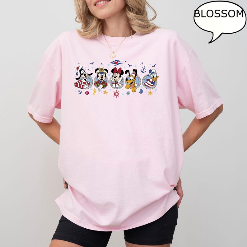 May include: A light pink t-shirt featuring a graphic of cartoon characters in nautical-themed circles. The characters include a dog, mouse, and duck. The word "BLOSSOM" is in a speech bubble.