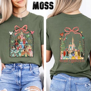 May include: Moss green t-shirt with a graphic of Disney princesses within a decorative arch and a pink bow. The back displays a castle and princesses with the words "Merry Christmas".