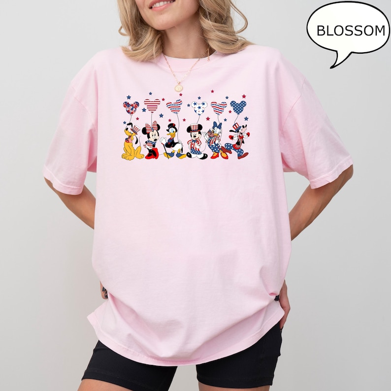 Puede incluir: Una camiseta rosa claro con un gr&aacute;fico de personajes de dibujos animados sosteniendo globos en forma de coraz&oacute;n con patrones rojos, blancos y azules. La palabra "BLOSSOM" est&aacute; en un bocadillo. La camiseta tiene mangas cortas.