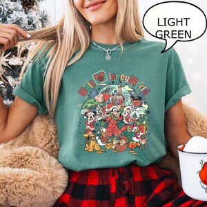 May include: Light green t-shirt featuring a colorful graphic of Disney characters in holiday attire, with the text "Walt Disney World". The shirt is paired with red and black plaid pajama pants.
