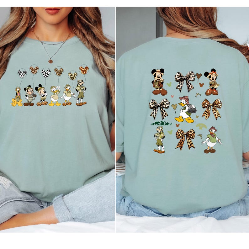 May include: A light blue t-shirt with a graphic print of Disney characters dressed in safari outfits. The front of the shirt features the characters in a line holding balloons. The back of the shirt features the characters with leopard print bows.
