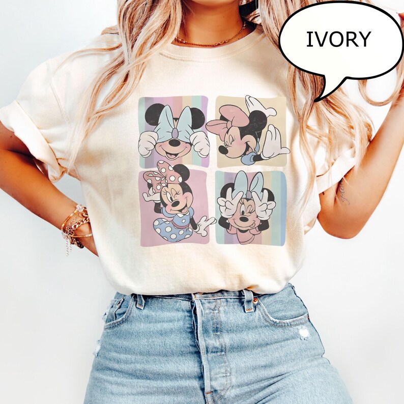 Puede incluir: Camiseta de color marfil con un gr&aacute;fico de cuatro paneles de Minnie Mouse en varias poses. Cada panel tiene un fondo de rayas pastel. La palabra "IVORY" est&aacute; en una burbuja de di&aacute;logo. La camiseta se combina con vaqueros azules.