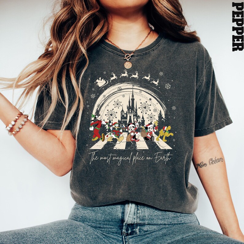 Puede incluir: Una camiseta gris oscuro con un gr&aacute;fico de estilo vintage de Mickey Mouse y sus amigos caminando por un paso de cebra frente al Castillo de Cenicienta en Disney World. El gr&aacute;fico incluye el texto "The most magical place on Earth".