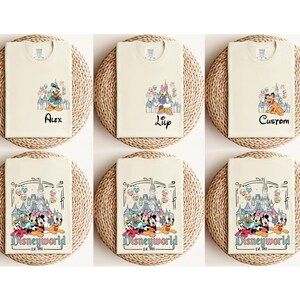 May include: Six cream-colored t-shirts with different Disney-themed designs. The designs include Mickey Mouse, Minnie Mouse, Donald Duck, Goofy, and Pluto. The shirts have the text "Disneyworld Est. 1965" and some have names like "Alex", "Lily", and "Custom".