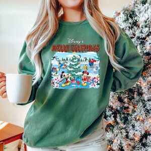May include: A green sweatshirt with a festive Disney Christmas design featuring Mickey Mouse, Minnie Mouse, Donald Duck, and other characters. The text "Disney's Merry Christmas" is printed in red on the sweatshirt.
