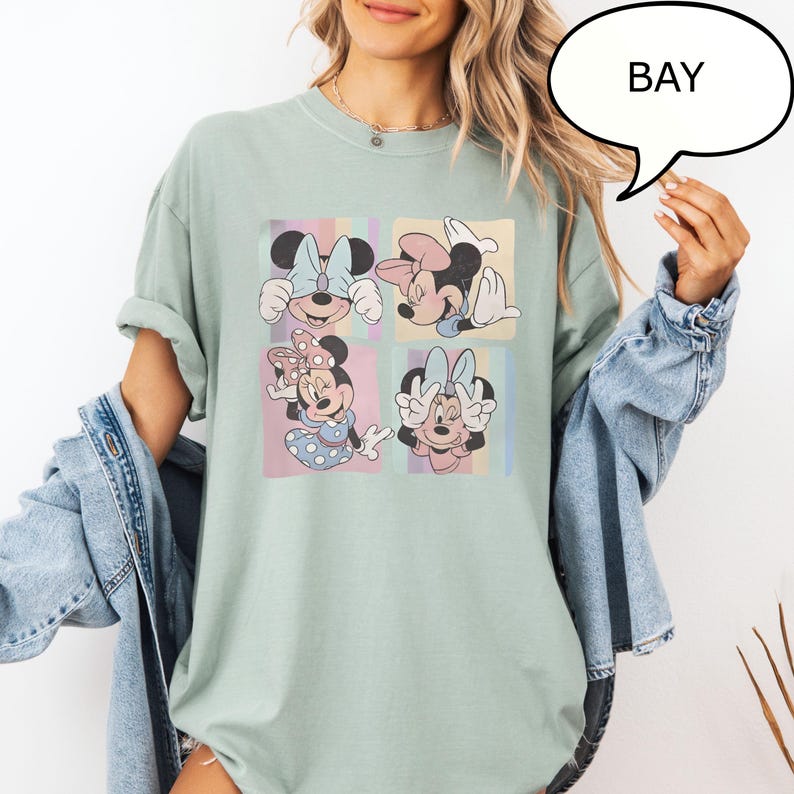 Puede incluir: Camiseta verde claro con un dise&ntilde;o de cuatro paneles de Minnie Mouse en varias poses. Cada panel tiene un fondo pastel con rayas verticales. La palabra "BAY" est&aacute; en una burbuja.
