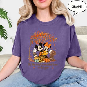 May include: A purple t-shirt featuring Mickey and Minnie Mouse embracing under a tree with autumn leaves. The shirt has a fall theme with pumpkins and the text "It's the most wonderful time of the year."
