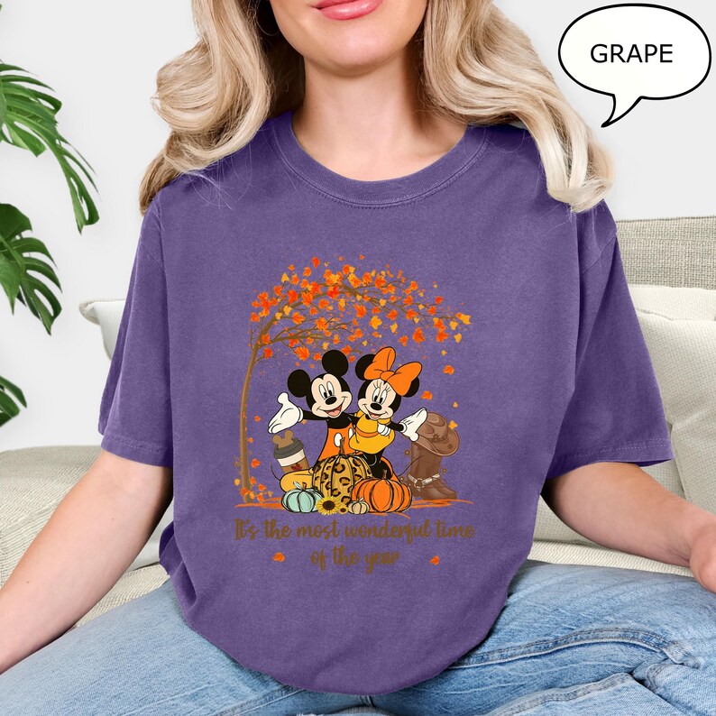 May include: A purple t-shirt featuring Mickey and Minnie Mouse embracing under a tree with autumn leaves. The shirt has a fall theme with pumpkins and the text "It's the most wonderful time of the year."
