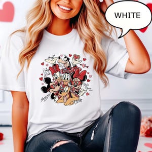 May include: White t-shirt with a colourful graphic of Disney characters, including Mickey and Minnie Mouse, Donald and Daisy Duck, Goofy, and Pluto, surrounded by red hearts. The word "WHITE" is in a speech bubble.