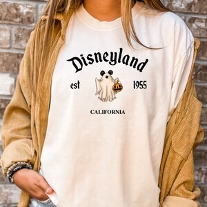Puede incluir: Camiseta blanca de manga larga con un gr&aacute;fico negro de un fantasma con orejas de Mickey Mouse sosteniendo una calabaza. El texto "Disneyland est 1955 CALIFORNIA" est&aacute; impreso en la camiseta.