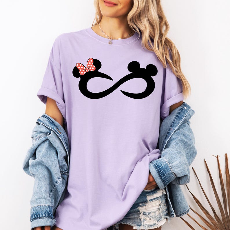K&ouml;nnte beinhalten: Ein lavendelfarbenes T-Shirt mit einem schwarzen Unendlichkeitszeichen und einer roten Schleife mit wei&szlig;en Punkten. Das Unendlichkeitszeichen hat auf der einen Seite einen Mickey-Maus-Kopf und auf der anderen Seite einen Minnie-Maus-Kopf.