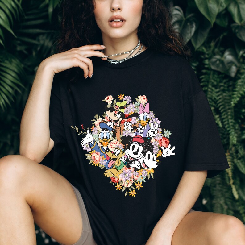 May include: Black t-shirt with a colourful floral print featuring Mickey Mouse, Minnie Mouse, Donald Duck, Goofy, and Pluto.