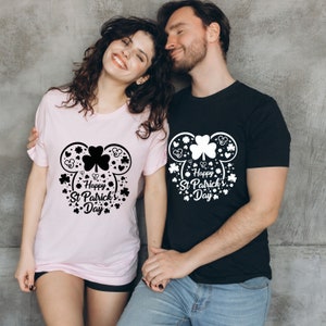 May include: A couple wearing matching black and pink t-shirts with a white graphic of a shamrock in a Mickey Mouse head design. The text on the shirts reads "Happy St. Patrick's Day".