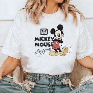 May include: White t-shirt with a black and white graphic of Mickey Mouse. The graphic includes the text "Mickey Mouse" and a signature.