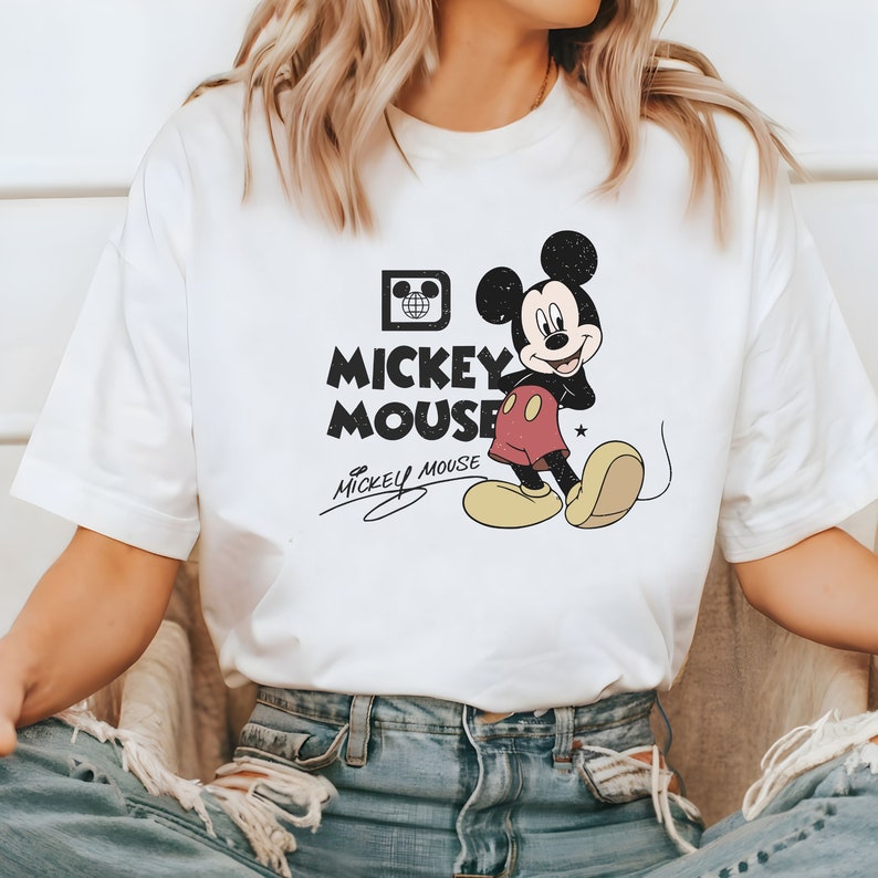May include: White t-shirt with a black and white graphic of Mickey Mouse. The graphic includes the text "Mickey Mouse" and a signature.