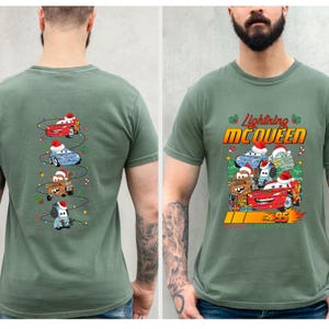 May include: Green t-shirt with a festive design featuring Lightning McQueen and other Cars characters wearing Santa hats. The front displays "Lightning McQueen" and "95". The back has a Christmas tree design with the Cars characters.