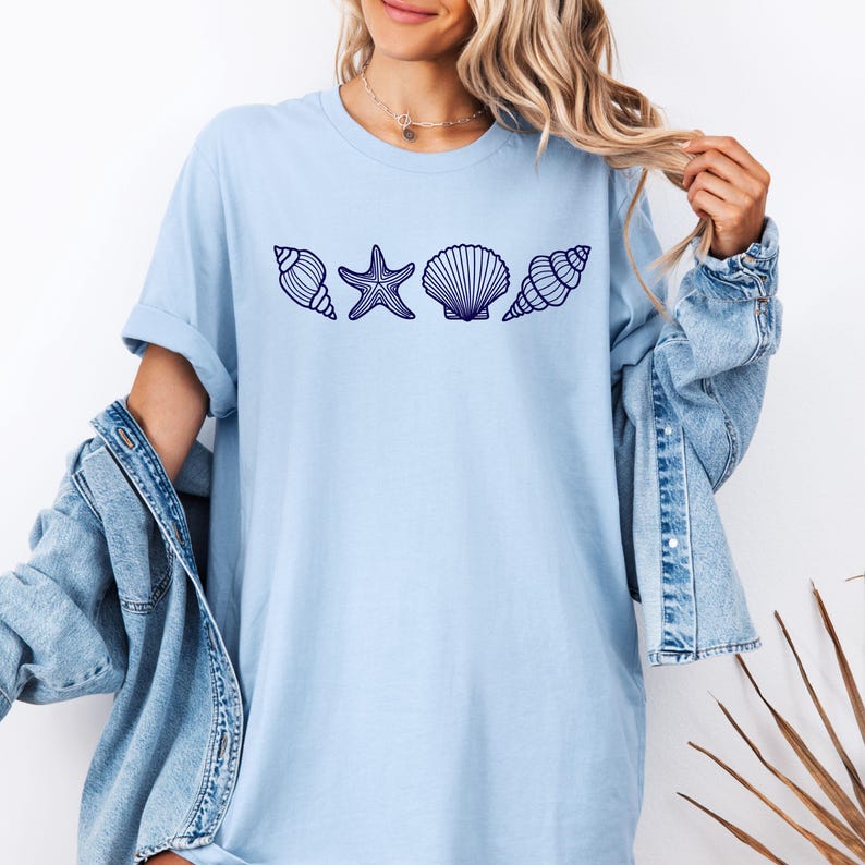 May include: A light blue t-shirt with a graphic of a starfish and seashells in a row.