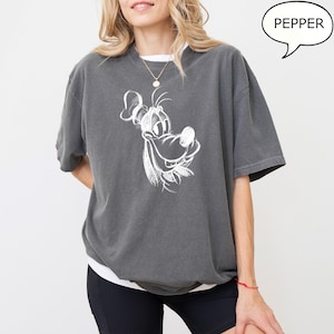 Puede incluir: Una camiseta gris antracita con un dibujo blanco de la cara de Goofy. El texto "PEPPER" est&aacute; en un bocadillo de di&aacute;logo en la esquina superior derecha de la imagen.