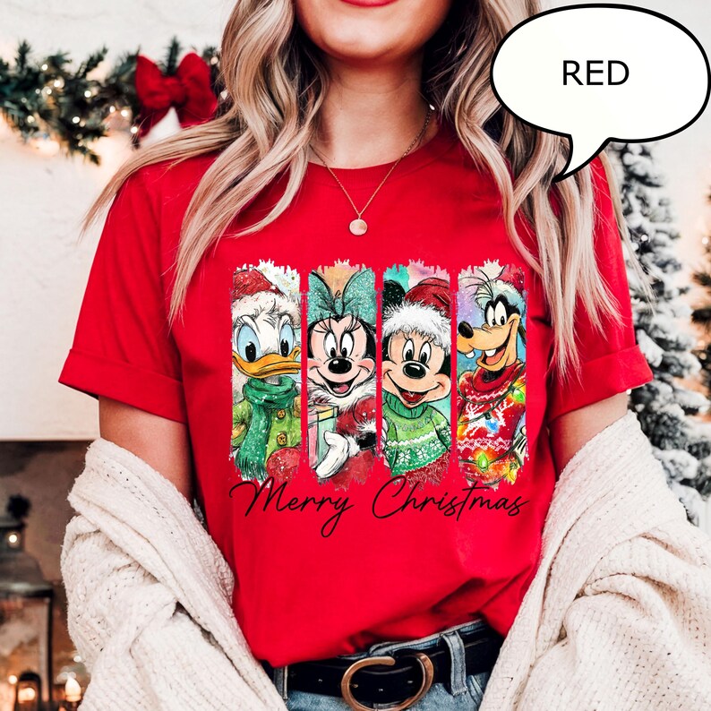 Puede incluir: Una camiseta roja con cuatro personajes de dibujos animados con atuendos navide&ntilde;os. Donald Duck, Minnie Mouse, Mickey Mouse y Goofy se muestran en paneles verticales. Las palabras "Merry Christmas" est&aacute;n escritas en cursiva debajo.