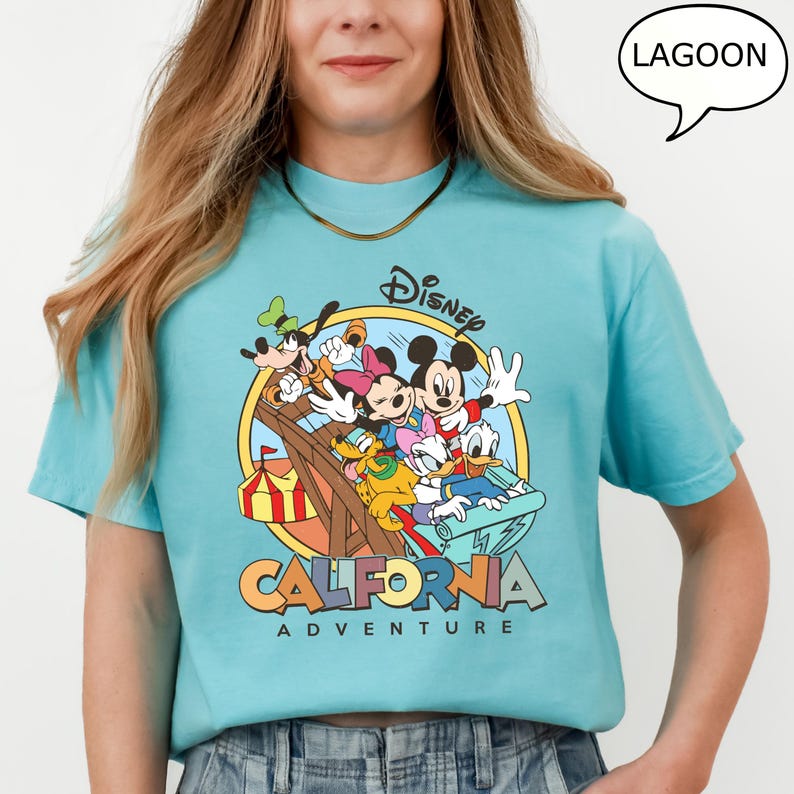Puede incluir: Una camiseta azul claro con un estampado gr&aacute;fico de Mickey Mouse y sus amigos montando una monta&ntilde;a rusa. El gr&aacute;fico incluye el texto "Disney California Adventure" y un bocadillo que dice "Lagoon".