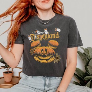 May include: A black cropped t-shirt with a vintage-style graphic of Mickey Mouse dressed as a pumpkin with the text "Disneyland" above him. There are also small ghost graphics on the shirt.