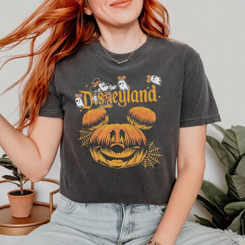 May include: A black cropped t-shirt with a vintage-style graphic of Mickey Mouse dressed as a pumpkin with the text "Disneyland" above him. There are also small ghost graphics on the shirt.