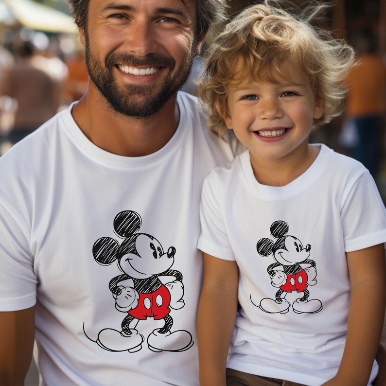 May include: A white t-shirt with a black and white sketch of Mickey Mouse wearing red shorts. The shirt is being worn by a man and a young boy.