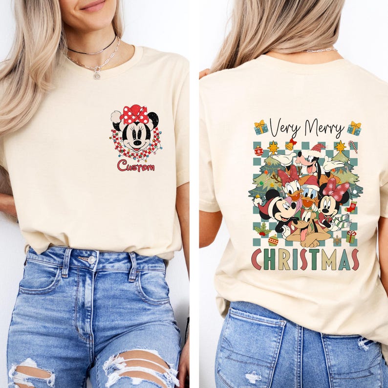 Pode incluir: Camiseta creme com um design de Natal da Minnie Mouse. A frente exibe um gr&aacute;fico da Minnie Mouse com a palavra "Custom" abaixo. A parte de tr&aacute;s mostra personagens da Disney e as palavras "Very Merry Christmas".
