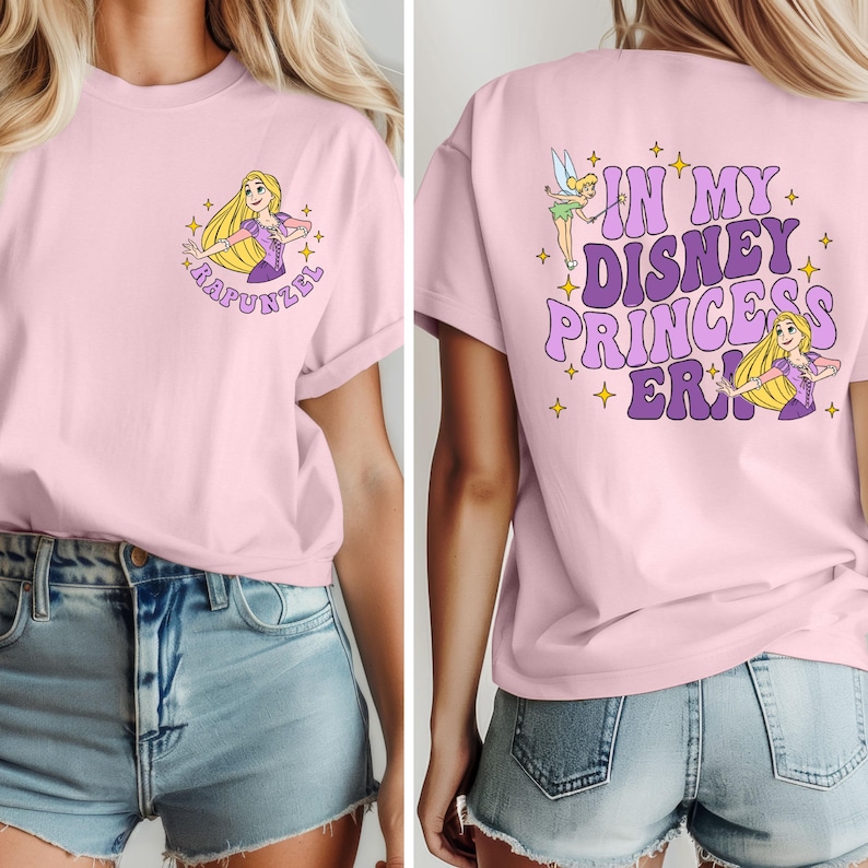 May include: Pink t-shirt with a graphic of Rapunzel on the front and the text "In My Disney Princess Era!" on the back. The shirt is being worn by a person with long blonde hair and denim shorts.
