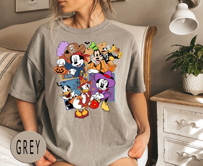K&ouml;nnte beinhalten: Ein graues T-Shirt mit einem bunten Grafikdruck von Mickey Mouse und seinen Freunden in Halloween-Kost&uuml;men. Die Grafik zeigt Mickey Mouse, Minnie Mouse, Donald Duck, Goofy und Pluto.