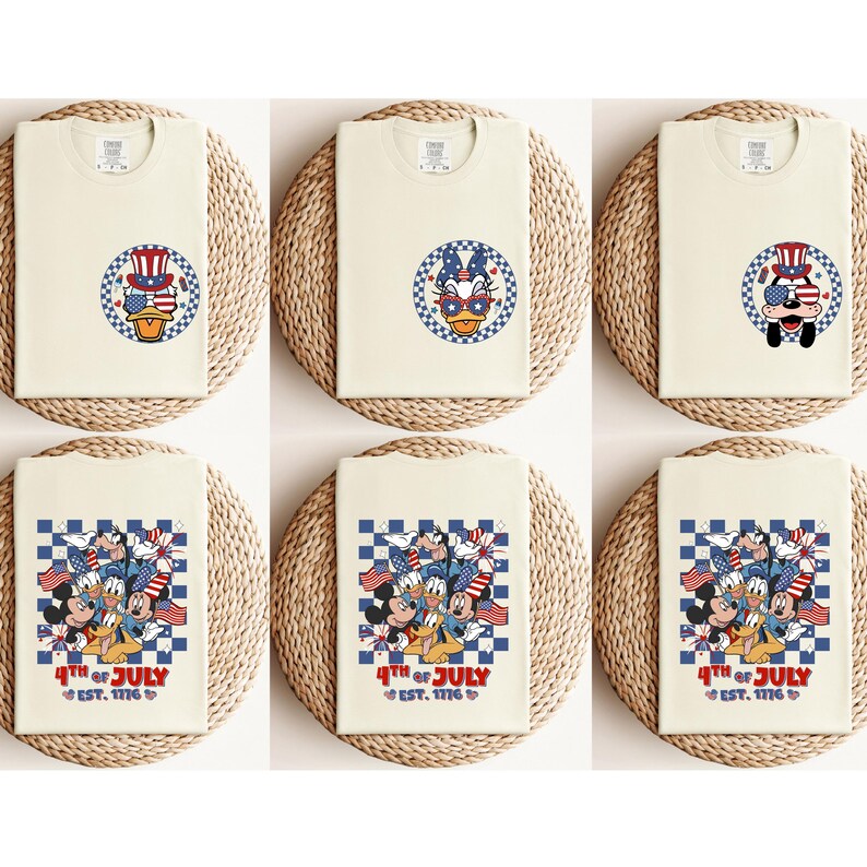 Pode incluir: T-shirts creme com desenhos de personagens de desenhos animados patri&oacute;ticos. Os desenhos incluem Pato Donald, Mickey Mouse e outros personagens usando chap&eacute;us e &oacute;culos de sol patri&oacute;ticos. O texto "4th of July EST. 1776" tamb&eacute;m est&aacute; presente.