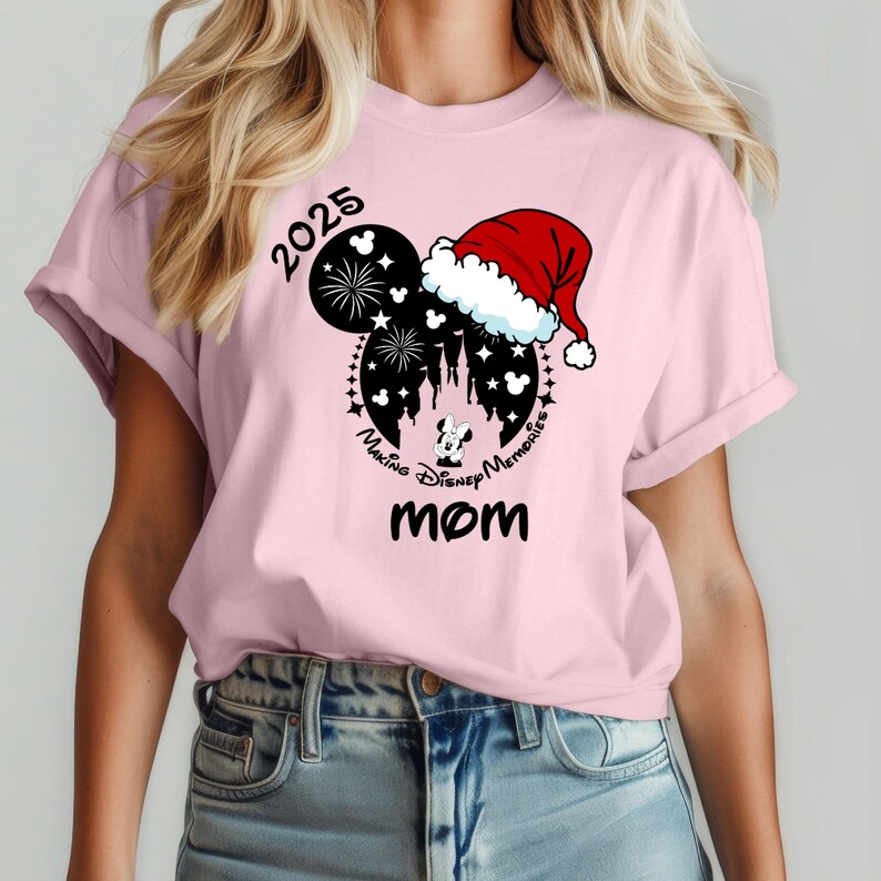 Peut inclure: T-shirt rose avec une silhouette noire et blanche de Mickey Mouse portant un bonnet de P&egrave;re No&euml;l. La silhouette comprend le texte "Making Disney Memories" et "2025". Le mot "MOM" est imprim&eacute; sous la silhouette.