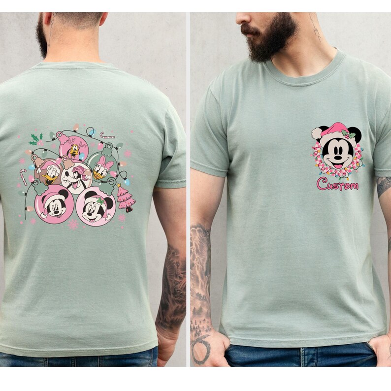 K&ouml;nnte beinhalten: Salbeigr&uuml;ne T-Shirts mit Mickey Mouse-Designs zum Thema Feiertage. Ein Shirt zeigt Mickey Mouse mit Weihnachtsm&uuml;tze, umgeben von Blumen und dem Wort "Custom". Das andere Shirt zeigt Mickey, Minnie, Donald und Daisy in Weihnachtskugeln.