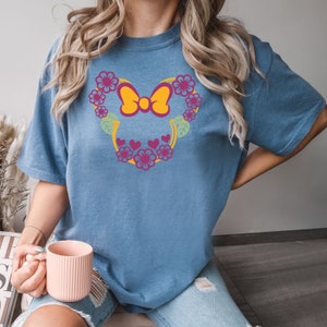 May include: A blue t-shirt with a floral design featuring a yellow bow. The design is reminiscent of a popular cartoon character.