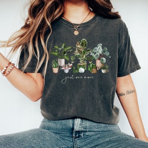 May include: A dark gray t-shirt with a graphic of potted plants and the text "just one more".