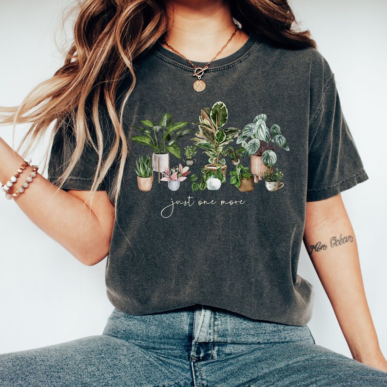 May include: A dark gray t-shirt with a graphic of potted plants and the text "just one more".