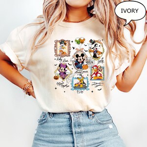 Puede incluir: Camiseta color marfil con personajes de Disney con tem&aacute;tica de Halloween enmarcados, incluyendo Mickey Mouse, Minnie Mouse, Donald Duck y Goofy. Cada personaje est&aacute; disfrazado para Halloween. La camiseta tiene la palabra "IVORY" en una burbuja.