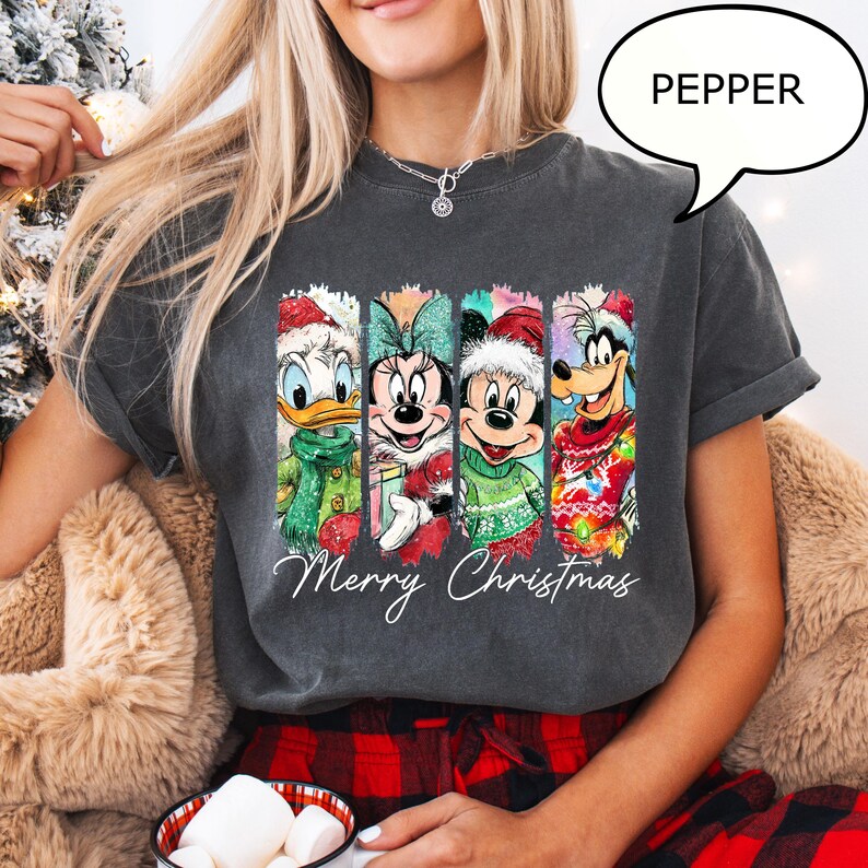 Puede incluir: Camiseta gris oscuro con cuatro personajes de Disney con atuendos navide&ntilde;os: Pato Donald, Minnie Mouse, Mickey Mouse y Goofy. Las palabras "Merry Christmas" est&aacute;n escritas debajo. La palabra "PEPPER" est&aacute; en una burbuja.
