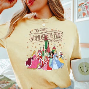 May include: A yellow t-shirt with a graphic of Disney princesses in front of a castle. The text "the most wonderful time of the year" is printed on the shirt.