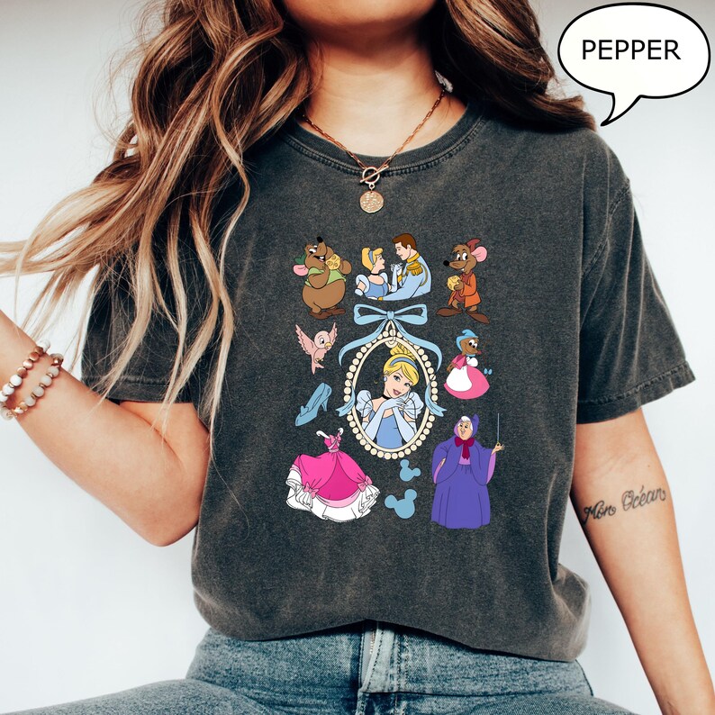Puede incluir: Camiseta gris oscuro con un collage tem&aacute;tico de Cenicienta. El dise&ntilde;o incluye a Cenicienta, su hada madrina, ratones y otros personajes. La palabra "PEPPER" est&aacute; en una burbuja.