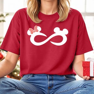 K&ouml;nnte beinhalten: Rotes T-Shirt mit einem wei&szlig;en Unendlichkeits-Symbol-Design, das eine Mickey Mouse und Minnie Mouse Kopf-Silhouette zeigt. Der Minnie Mouse Kopf hat eine rote Schleife mit wei&szlig;en Punkten.