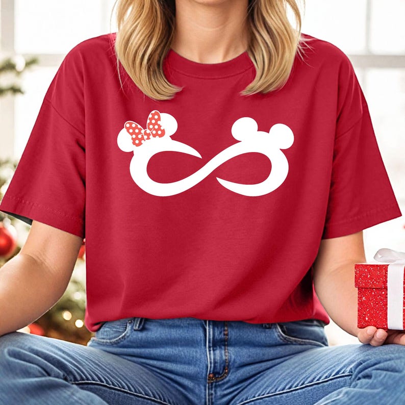 K&ouml;nnte beinhalten: Rotes T-Shirt mit einem wei&szlig;en Unendlichkeits-Symbol-Design, das eine Mickey Mouse und Minnie Mouse Kopf-Silhouette zeigt. Der Minnie Mouse Kopf hat eine rote Schleife mit wei&szlig;en Punkten.