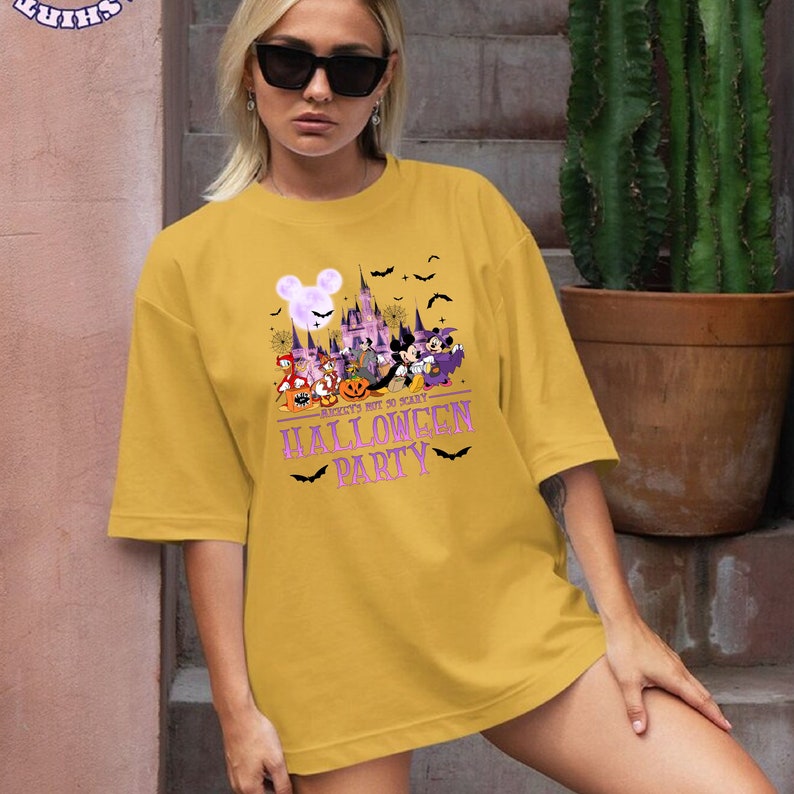 May include: A yellow t-shirt with a graphic of Mickey Mouse and friends in front of the Cinderella Castle. The text "Mickey's Not So Scary Halloween Party" is printed in purple on the shirt.