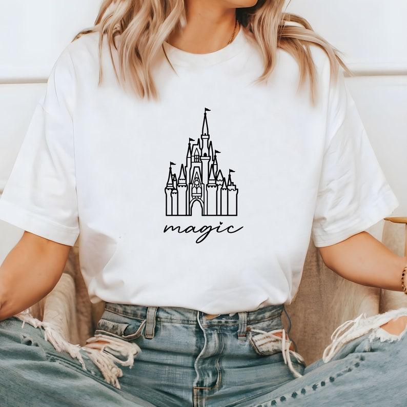 May include: White t-shirt with a black outline of a castle and the word "magic" written underneath.