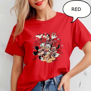 May include: Red t-shirt with a graphic of Disney characters, including Mickey and Minnie Mouse, Donald and Daisy Duck, and Goofy. The graphic includes hearts and text. A speech bubble above the shirt says "RED".