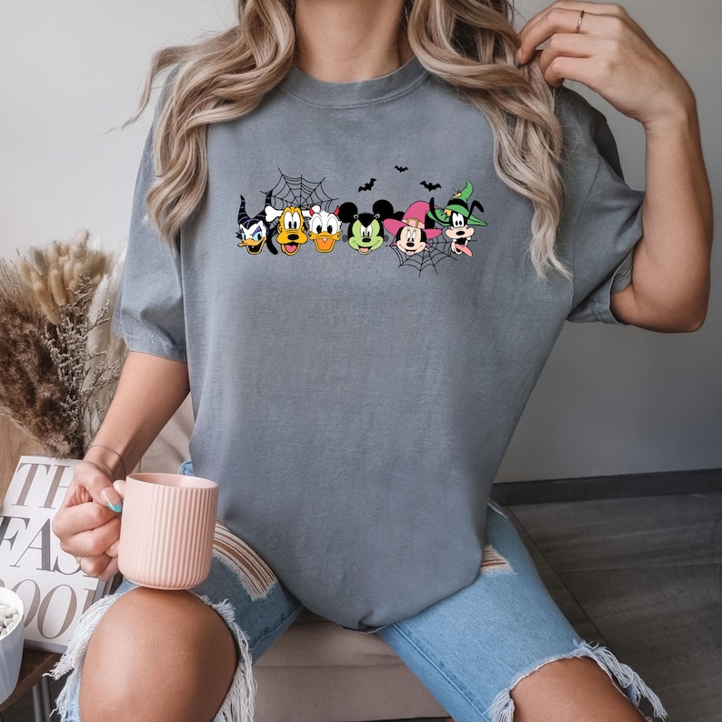 May include: Grey t-shirt featuring a graphic of Mickey Mouse and his friends dressed in Halloween costumes. The graphic includes Mickey Mouse, Minnie Mouse, Donald Duck, Goofy, and Pluto.