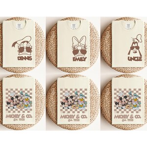 May include: Six cream-colored t-shirts with brown graphics. Three shirts feature cartoon characters with sunglasses and names: "DENNIS", "EMILY", and "UNCLE". The other three shirts have a checkered design with "MICKEY & CO. Est. 1928" and cartoon characters.