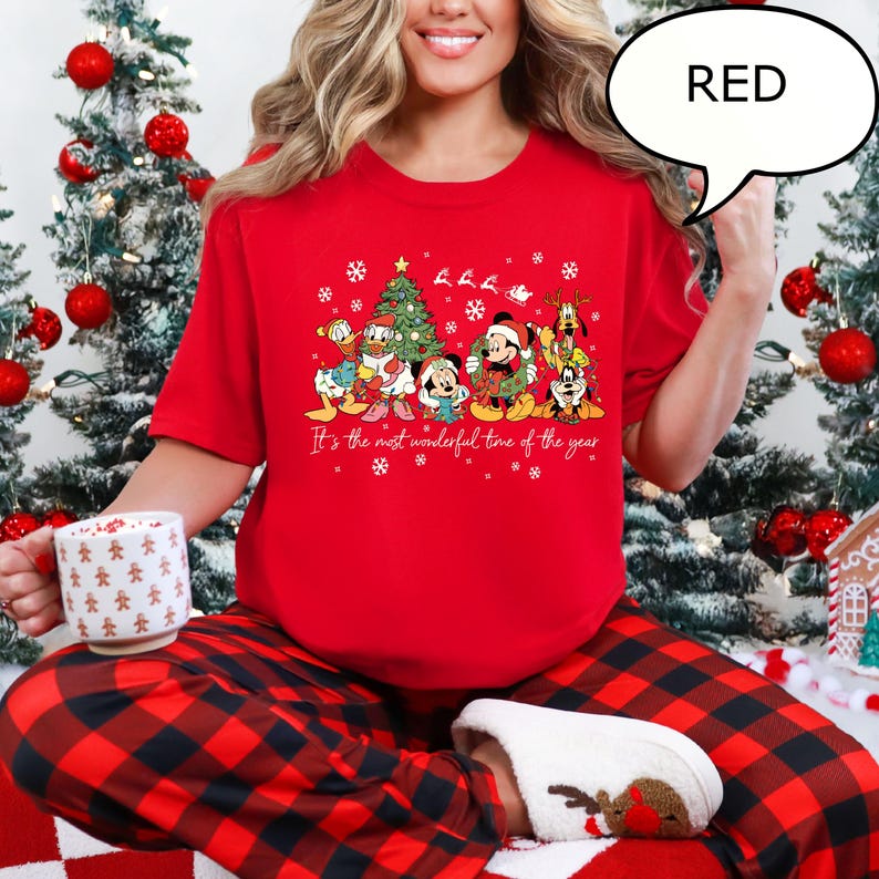 May include: A red Christmas t-shirt featuring Disney characters, including Mickey Mouse, Donald Duck, and Goofy, with a Christmas tree and the text "It's the most wonderful time of the year." The shirt is paired with red and black plaid pajama pants.